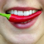 Man sieht den Mund einer Frau  Zwischen den Zähnen klemmt eine Chli Schote