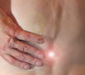 Eine Hand liegt auf einer schmerzenden Stelle am unteren Rücken