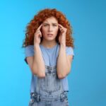 Eine junge rothaarige Frau hält sich die Hände an den Kopf