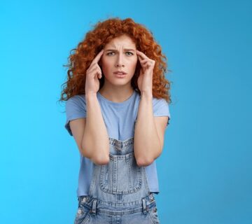Eine junge rothaarige Frau hält sich die Hände an den Kopf